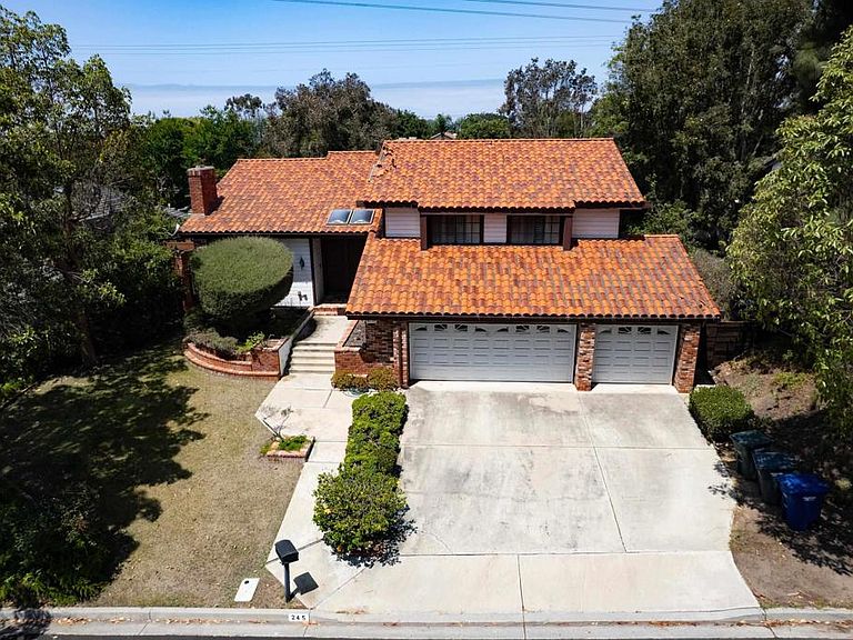 Top-down drone view of the terracotta tile roof and the long driveway leading to the three-car garage, framed by mature trees